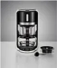 A modern coffee maker with glass carafes and black accents, placed on a white countertop next to a scoop and a small bowl. Náhled obrázku produktu