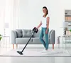 A woman is vacuuming a living room with a cordless vacuum cleaner. Produktbild-Vorschau