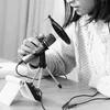 A person is using a microphone with a pop filter and a tripod stand, connected to a smartphone on a stand, with headphones nearby. Anteprima dell’immagine prodotto