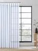 A white sheer curtain hangs in front of a large window with black mullions, revealing trees outside. Produktbild-Vorschau