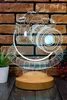 A 3D LED lamp shaped like a camera, displayed on a wooden base against a brick wall background. Produktbild-Vorschau