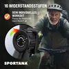 An older man riding a stationary bike outdoors, with a close-up of the tension control dial. Produktbild-Vorschau