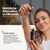 A woman holds a dropper bottle of hair oil, with text overlay about its benefits. Produktbild-Vorschau