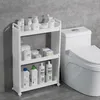 A white three-tier rolling storage cart filled with various bathroom products is placed next to a white toilet in a bathroom with gray tiled walls. Produktbild-Vorschau