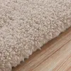 A close-up view of a beige carpet with a textured surface, placed on a wooden floor. Podgląd zdjęcia produktu