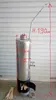 A stainless steel wood-fired water heater with dimensions marked on it, placed on a concrete floor in front of a corrugated metal wall. Produktbild-Vorschau