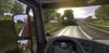 View from inside a truck cab, looking out at a road and scenery. A signpost indicates a town name. Produktbild-Vorschau