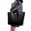 A person is holding a black quilted tote bag. Náhľad obrázku produktu