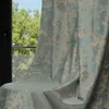 A close-up of a curtain with a textured pattern, partially covering a window with greenery visible outside. Produktbild-Vorschau