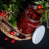 A jar of homemade jam with fresh berries and leaves on a rustic rope mat. Podgląd zdjęcia produktu