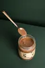 A jar of hazelnut spread with a spoon scooping some out, set against a dark green background. Produktbild-Vorschau