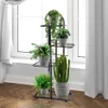 A black metal plant stand with multiple tiers holding various potted plants in front of a window with white curtains. Náhled obrázku produktu
