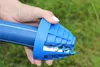 A hand holding a blue pipe chamfering tool against a blurred green grassy background. Voir les images du produit