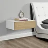 A floating nightstand with a drawer is mounted on a gray wall next to a white bed. Náhled obrázku produktu