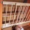 A baby is at the bottom of a wooden staircase, with a wooden baby gate installed at the top of the stairs. Voir les images du produit