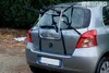 A silver Toyota Yaris car with a black and silver bike rack mounted on the rear, parked outdoors with a natural background of trees and foliage. Anteprima dell’immagine prodotto
