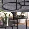 A close-up view of two round coffee tables with black marble tops and black metal legs, placed on a textured gray rug. One table holds a vase of white roses and a diffuser, while the other displays two geometric vases. Náhľad obrázku produktu