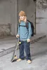 A young person stands with a skateboard and backpack in an urban environment. Produktbild-Vorschau