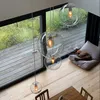 A modern interior with large windows overlooking a garden, featuring a cluster of glass pendant lights and a dog resting on a cushion. Produktbild-Vorschau