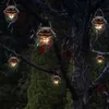 Several solar-powered lanterns hanging from tree branches at dusk. Produktbild-Vorschau