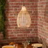 A hanging lamp made of rattan is shown above a dining table with brick walls in the background. Produktbild-Vorschau