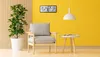 A modern living room scene with a chair, plant, and a digital clock on a yellow wall. Produktbild-Vorschau
