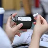 A person's hands are holding a black AirPods case and one earbud. Anteprima dell’immagine prodotto