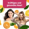 Two women are smiling and touching their hair, surrounded by oranges and leaves, with a pink banner at the top. Produktbild-Vorschau