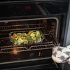 A glass baking dish filled with broccoli and red peppers is being placed into an oven. Anteprima dell’immagine prodotto