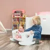 A young girl plays with a doll in a doll bed next to a dollhouse. Produktbild-Vorschau