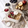 A lunchbox filled with berries, yogurt, and granola, surrounded by fresh fruits and cutlery. Podgląd zdjęcia produktu