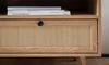 Close-up of a wooden TV cabinet drawer with a rattan front and a black handle. Produktbild-Vorschau