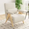 A cream-colored lounge chair with wooden accents is placed on a patterned rug in a well-lit room with a large window and a plant. Produktbild-Vorschau