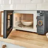 A microwave oven with its door open, showing a bowl of food inside, placed on a wooden countertop. Anteprima dell’immagine prodotto