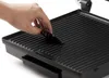 A hand is shown cleaning the grill plate of a contact grill with a small black cleaning tool. Podgląd zdjęcia produktu