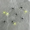 Several black and yellow plastic spiders are scattered on a white, wispy spider web. Produktbild-Vorschau