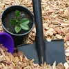 A small plant in a pot, a shovel, and a purple bucket are placed on a bed of wood chips. Produktbild-Vorschau