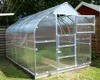 A greenhouse with its doors and windows open, set up in a grassy yard with trees and a red building in the background. Produktbild-Vorschau