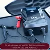 A black AEG battery charger with red and black clamps is shown on a dark surface. Produktbild-Vorschau