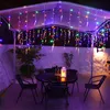 An outdoor patio area at night, decorated with colorful icicle string lights hanging from a canopy over a table and chairs. Produktbild-Vorschau