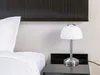 A bedside lamp on a nightstand next to a bed. Produktbild-Vorschau