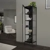 A tall, narrow black display cabinet with glass doors stands in a modern living room setting, showcasing various items on its shelves. A white armchair is visible in the background. Podgląd zdjęcia produktu