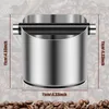 A close-up shot of a stainless steel espresso knock box with measurement markings in centimeters and inches overlaid on the image. The background consists of coffee beans, with a few beans also in the foreground. Produktbild-Vorschau