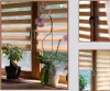 A collage of images showing a creme-colored double roller blind with wooden window frames and plants. Produktbild-Vorschau