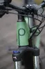 A close-up shot of the front of a green e-bike, showing the handlebars, front fork, and a prominent logo. Produktbild-Vorschau