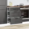 A close-up view of a black kitchen cabinet with three drawers, one of which is partially open, revealing the interior. The cabinet is set against a white tiled backsplash and a wooden countertop. Náhled obrázku produktu