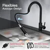 A black kitchen faucet with a flexible pull-out hose is shown over a stainless steel sink, with water spraying from the hose. Anteprima dell’immagine prodotto