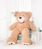 A large teddy bear sitting on a chair in a room with a lamp and side tables. Anteprima dell’immagine prodotto