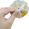 A hand is holding open a circular container filled with small golden rings. Produktbild-Vorschau