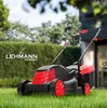 A red and black electric lawnmower is shown on a green lawn in front of a hedge and a house. Produktbild-Vorschau